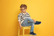 © Africa Studio - Cute stylish boy sitting on chair near color wall