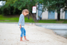 Adorable Little Girl Walking Along White Sand Near The Lake