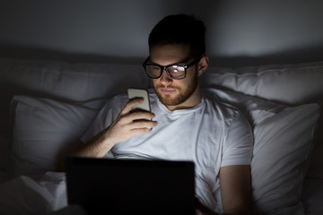 Wall Mural - man with laptop and smartphone at night in bed