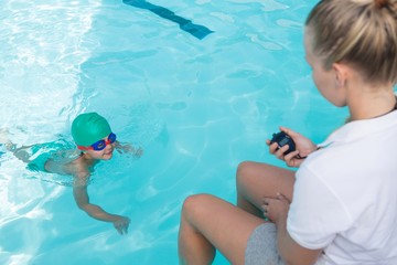 Female trainer monitoring time of boy swimming in pool