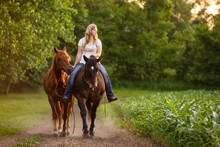 Woman Riding Horse While Another Horse Walking Beside On Dirt Road