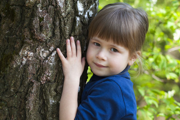 Poster - Lovely smiling little girl standing near big tree on green grass on a sunny day