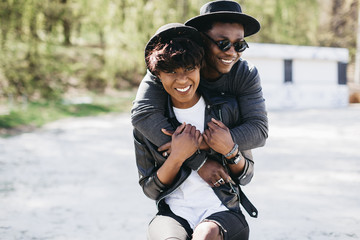 A beautiful and stylish young african couple in sunglasses and hats embracing on a outdoor of summer.