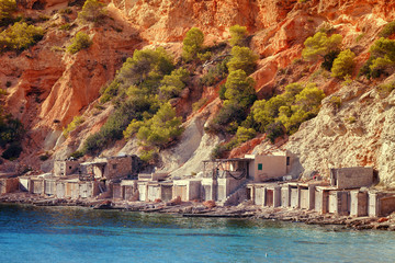 Wall Mural - Old fishing huts where they keep the run of fishing vessels in the Caleta Beach in Ibiza, with its red earth, Spain.