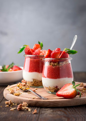 Delicious homemade granola, yogurt and strawberry parfait in glass jars on rustic wooden background