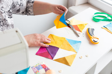 Wall Mural - needlework and quilting in the workshop of a woman tailor on white background - hands of tailor woman at work with pieces of colored fabric on the table with threads, fabrics, needles, cutters