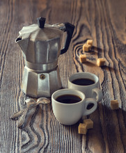 Two Cups Of Coffee With Pieces Of Cane Sugar And Italian  Coffee Maker On Wooden Table.  Toned Image.