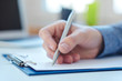 © cameravit - Male hand holding silver pen ready to make note in a clipboard. Businessman or employee at workplace writing business ideas, plans or tasks. Office life or education concept.