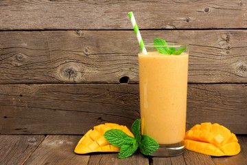 Wall Mural - healthy mango smoothie in a glass with mint and straw against a rustic wood background