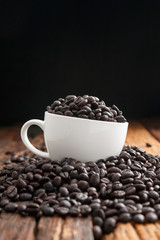 Wall Mural - Close up shot of dark roasted coffee bean in white ceramic cup on wooden floor with copy space