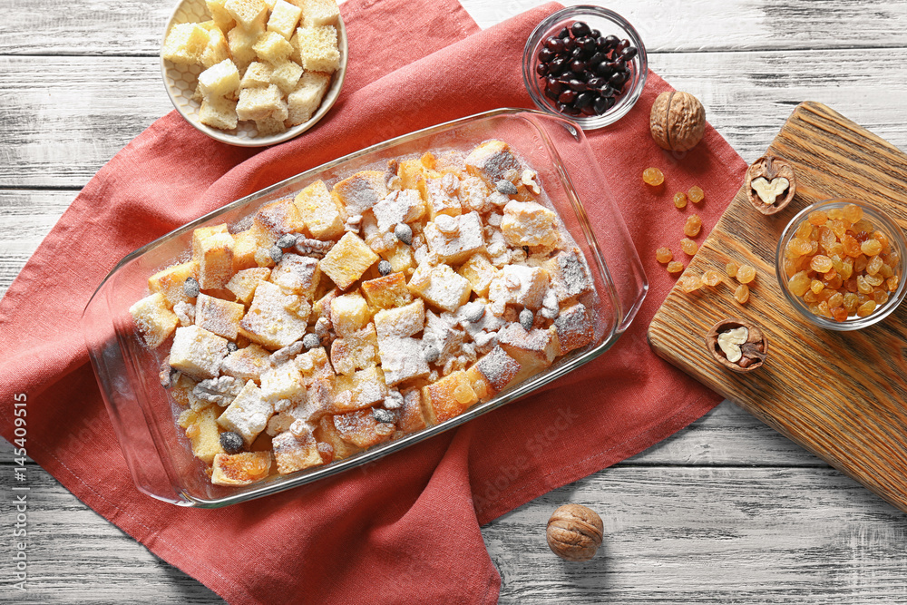 Bread pudding with raisins, walnuts and sugar powder in baking dish on table