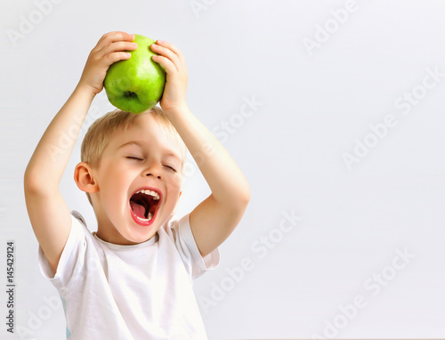 Fotografía small boy holds a big green apple, healthy food and vitamins, smiling, white bac
