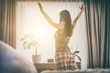 © REDPIXEL - Young woman stretches out in the morning after waking up looking out the window.