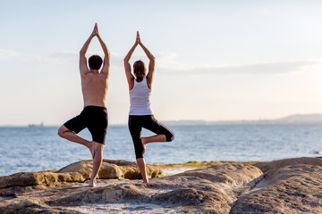 Wall Mural - A couple is doing yoga exercises at the seashore of Mediterranean sea