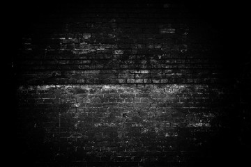 An old gloomy brick wall. Dark lighting, a light spot in the center of the brickwork. Black white empty space. Grunge background