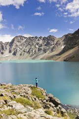 girl in blue jacket standing with hands-up above blue lake in mountains