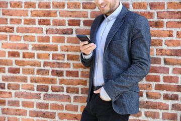 Wall Mural - young casual business man using smartphone in urban city background relaxing on brick wall texting s
