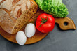 Eggs, tomato, lettuce leaves, bread. Wooden board with Ingredients for cooking. From above.