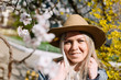 Attractive young blond girl in a hat smiles among the spring flowers closeup
