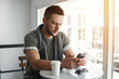 © Cookie Studio - Closeup of guy sitting at table in cafe, texting message.