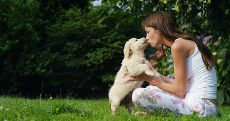 A young woman on a sunny day playing with his Golden Retrivier puppy in the garden giving himself kisses with love and affection	