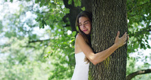 On A Sunny Day A Woman Embracing The Tree As A Sign Of Love For Nature. Nature That She Loves And Protects Because The Tree Is A Symbol Of Life. The Naturalist Woman Is Carefree And Smiling