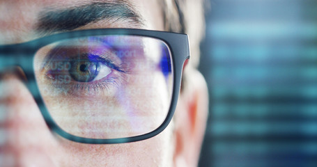 Close up of young businessman with blue eyes wearing the glasses looking on the waveform lines and data	