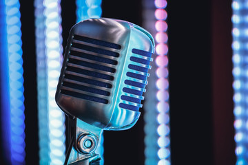 Retro style microphone on stage in the spotlight performance of the musical group. Microphone for rock music. Microphone in blue light og stage. Music is in the air. Color background.