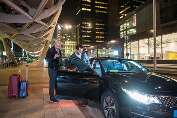 Driver Assisting Passenger Entering Car On City Street