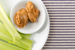 Celery stalks with peanut butter on a white plate atop a blue striped tablecloth.