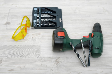 Wall Mural - A cordless drill set on a wooden table background with a set of bits in the box and yellow protective glasses around.