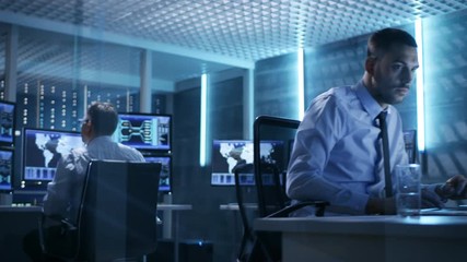 Poster - Two Technical Engineers at Sitting at Their Workplaces With Multiple Displays. They're in Monitoring Room with Servers.  Shot on RED EPIC-W 8K Helium Cinema Camera.