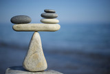 Fototapeta  - Balance of stones. To weight pros and cons. Balancing stones on the top of boulder. Close up. Balance of stones on a blue sky background with a copy space. Scales. Stones balance, sustainability.