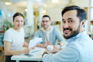 Canvas Print - Team of cheerful business people smiling and looking at camera while meeting at table in modern office, enjoying work