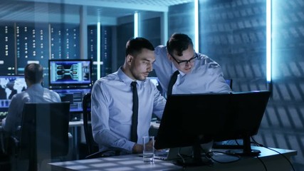 Poster - Two Operation Engineers Working on Solving Problems in System Control Room. In the Background Their Colleague, Displays and Server Racks.  Shot on RED EPIC-W 8K Helium Cinema Camera.