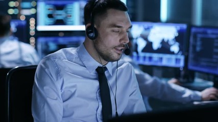 Poster - In System Control Center Technical Support Specialist Speaks into Headset. His Colleagues are Working in the Background in a Room Full of Screens.  Shot on RED EPIC-W 8K Helium Cinema Camera.