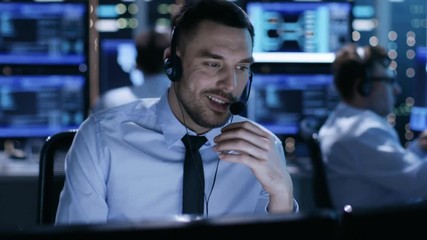 Poster - In System Control Center Technical Support Specialist Speaks into Headset. His Colleagues are Working in the Background in a Room Full of Displays.  Shot on RED EPIC-W 8K Helium Cinema Camera.