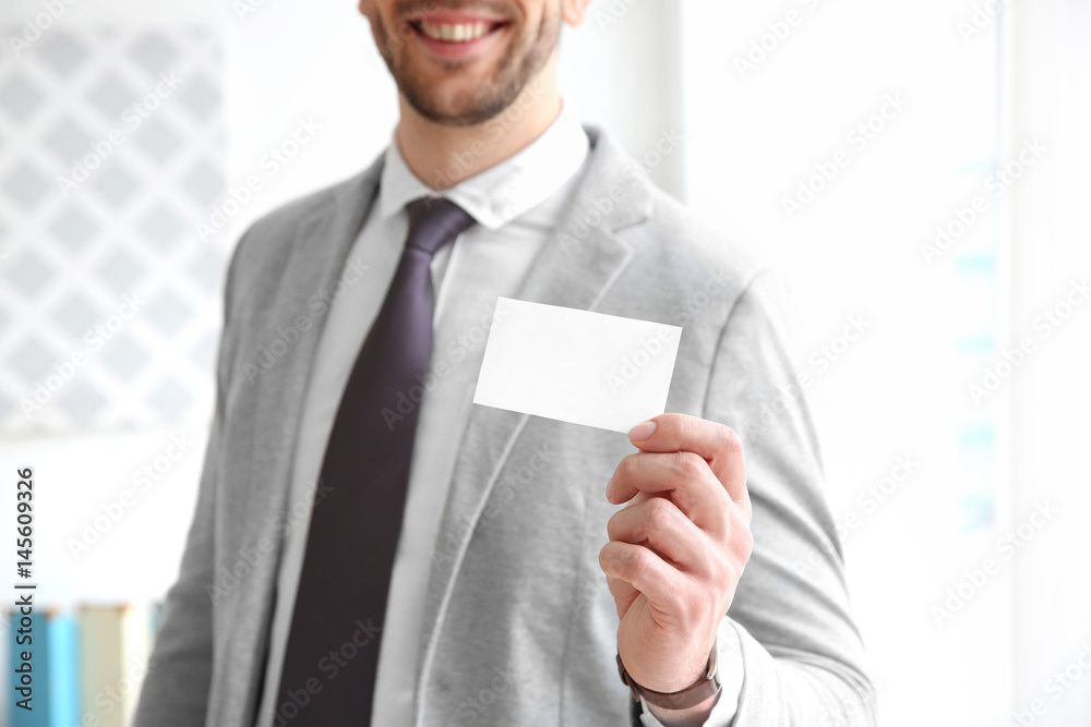 Handsome young man with business card on blurred background, closeup