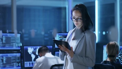 Aufkleber - Young Female Engineer Uses Tablet in System Control Center. In the Background Her Coworkers are at Their Workspaces with many Displays Showing Valuable Data.