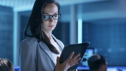 Aufkleber - Young Female Government Employee Wearing Glasses Uses Tablet in System Control Center. In the Background Her Coworkers are at Their Workspaces with many Displays Showing Valuable Data. 