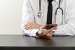 close up of smart medical doctor working with smart phone and stethoscope on dark wooden desk