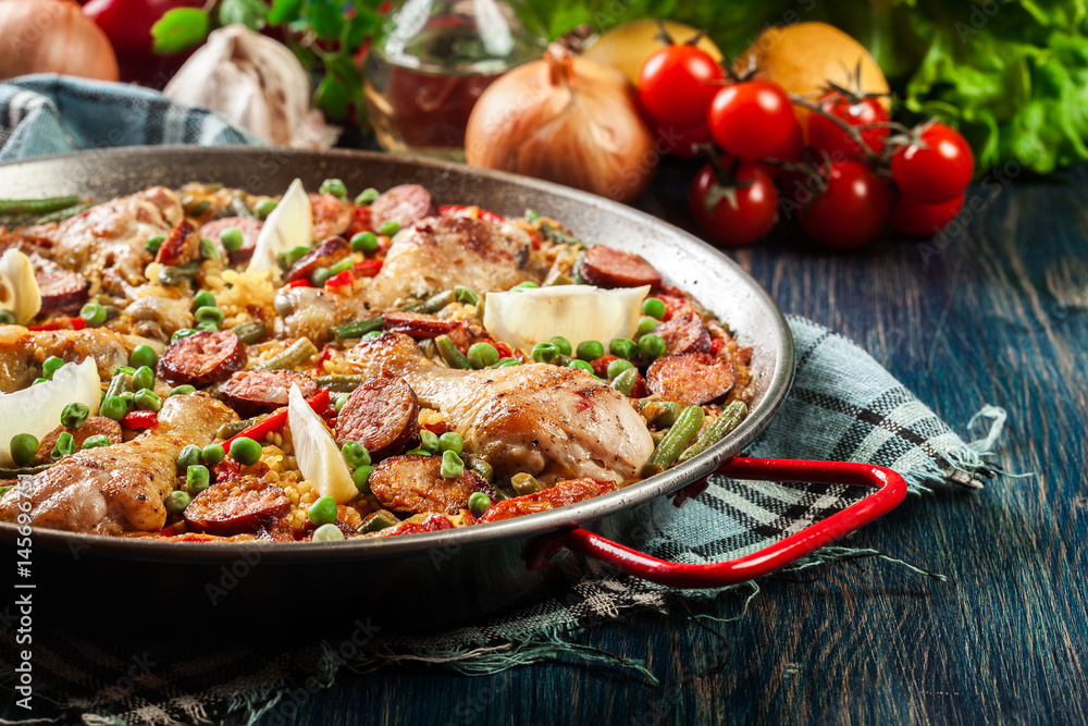 Traditional paella with chicken legs, sausage chorizo and vegetables served in paellera