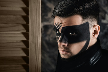 Wall Mural - fantasy art makeup. man with black painted mask on face. Close up Portrait. Professional Fashion Makeup.