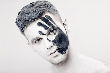 Wall Mural - Young man with black hand print on white face. Closeup Portrait.  Professional Fashion Makeup. fantasy art  makeup