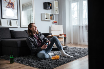 Happy man sitting at home indoors play games with joystick