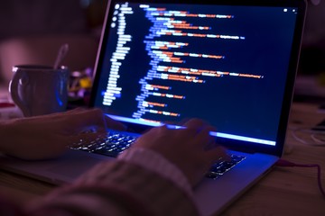 Hacker or developer programming code script late at night hours. HTML, CSS or java script on a laptop computer screen.