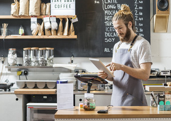 Young bartender using tablet while standing behind counter in cafe 