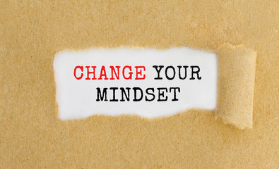 Poster - text change your mindset appearing behind ripped brown paper.