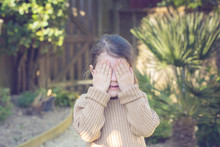 Little Girl Playing Hide And Seek In The Garden, Holding Her Hands In Front Of Her Eyes