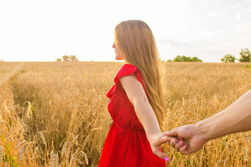 Follow me, Beautiful young woman holds the hand of man in a wheat field